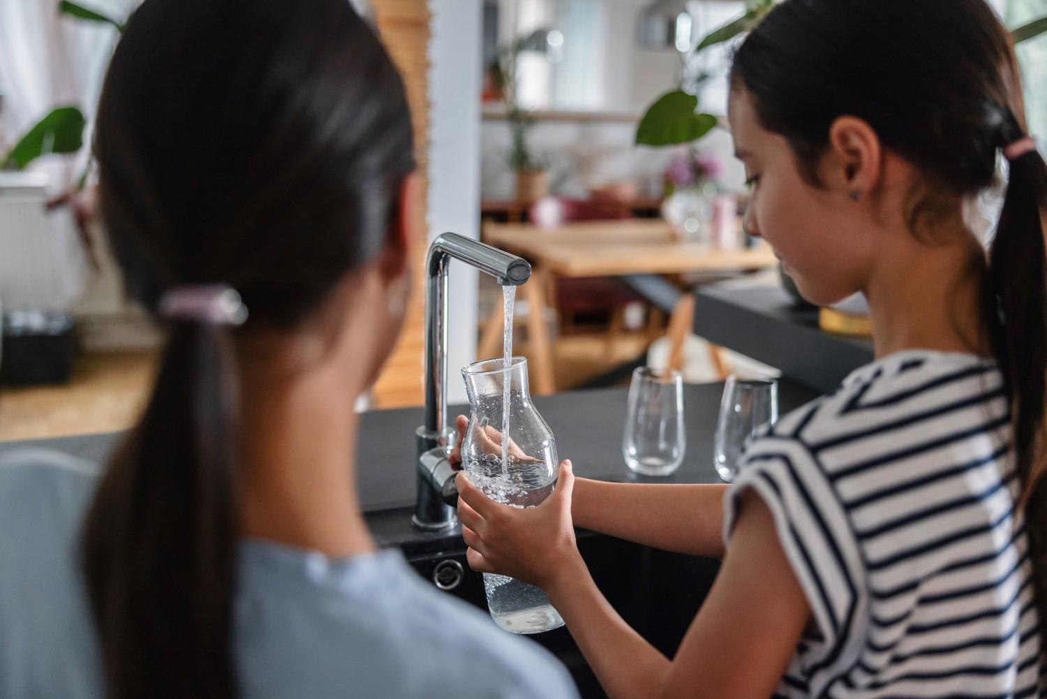 Young girls filling up a jug of water from the kitchen tap