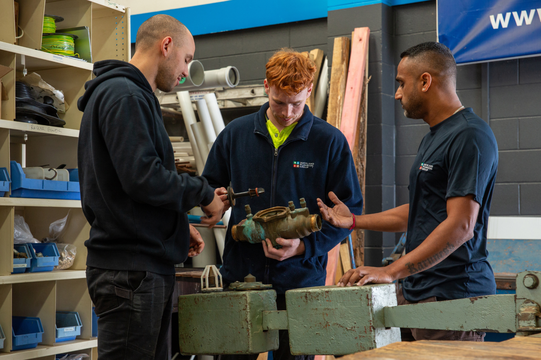 Three apprentice plumbers learning how to fix a plumbing fitting